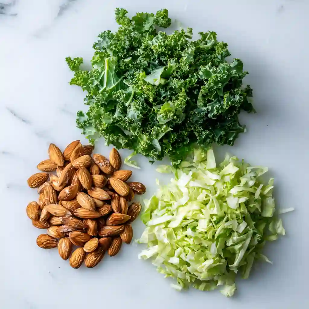 Chick Fil A Kale Salad Recipe (Copycat) - Crunchy, Fresh & So Easy to Make 5 Flat lay of curly kale, shredded cabbage, and roasted almonds arranged clearly on a white surface
