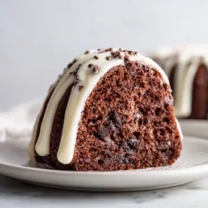 A slice of chocolate chocolate chip Nothing Bundt Cake served on a plate with cream cheese frosting