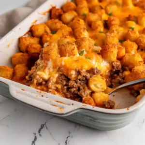 A square serving of tater tot casserole on a plate with beef and melted cheddar
