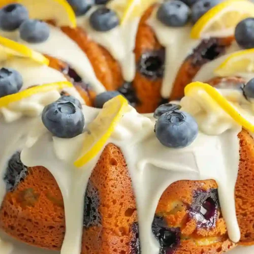 Homemade blueberry lemon bundt cake with cream cheese frosting, topped with fresh blueberries and lemon slices.