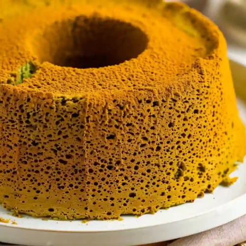 Close-up of a homemade matcha chiffon cake with a soft, airy texture and a slice cut out, served on a white plate.