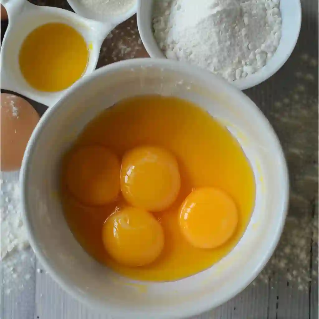 Bowl with egg yolks, flour, and baking powder arranged on a wooden table in natural light