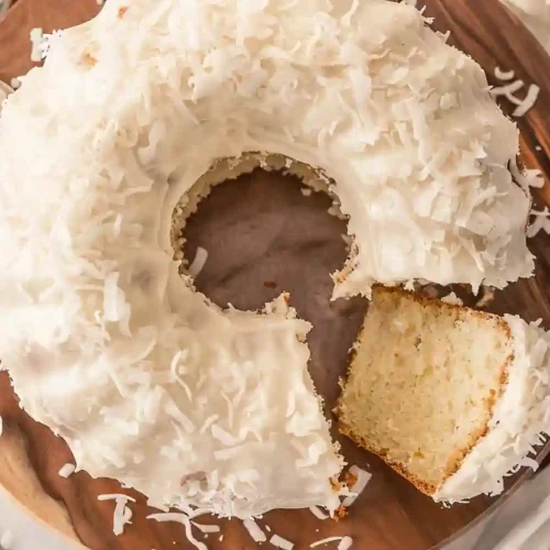 The Best Coconut Bundt Cake You’ll Ever Bake 8 Coconut Bundt Cake topped with creamy coconut buttercream and shredded coconut on a wooden cake stand