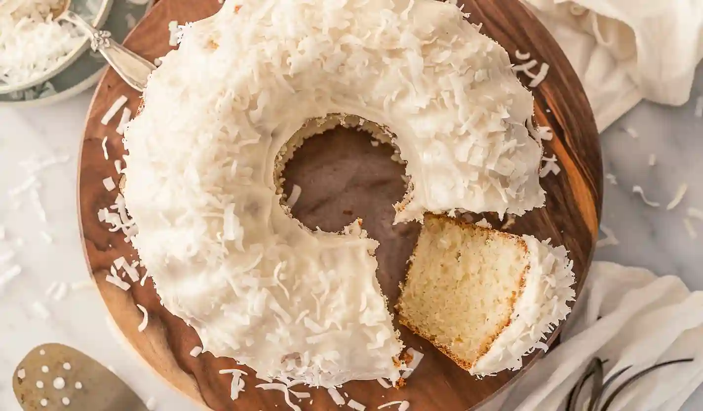 21 Nothing Bundt Cake Copycat Recipes (Super Moist + Bakery Style) 2 Coconut Bundt Cake topped with creamy coconut buttercream and shredded coconut on a wooden cake stand