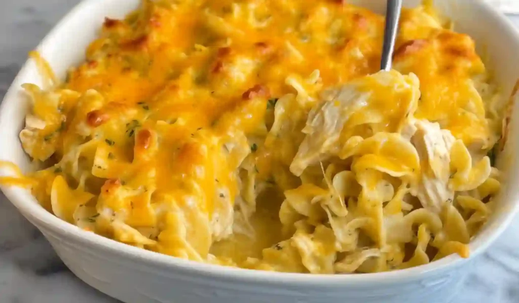 Close-up of a baked chicken noodle casserole in a white dish with melted cheddar on top.