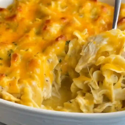Close-up of a baked chicken noodle casserole in a white dish with melted cheddar on top.