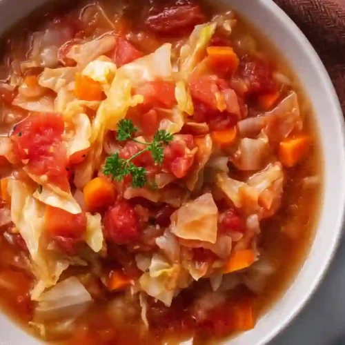 Close-up of homemade cabbage soup with tomatoes, carrots, and cabbage in a rustic bowl