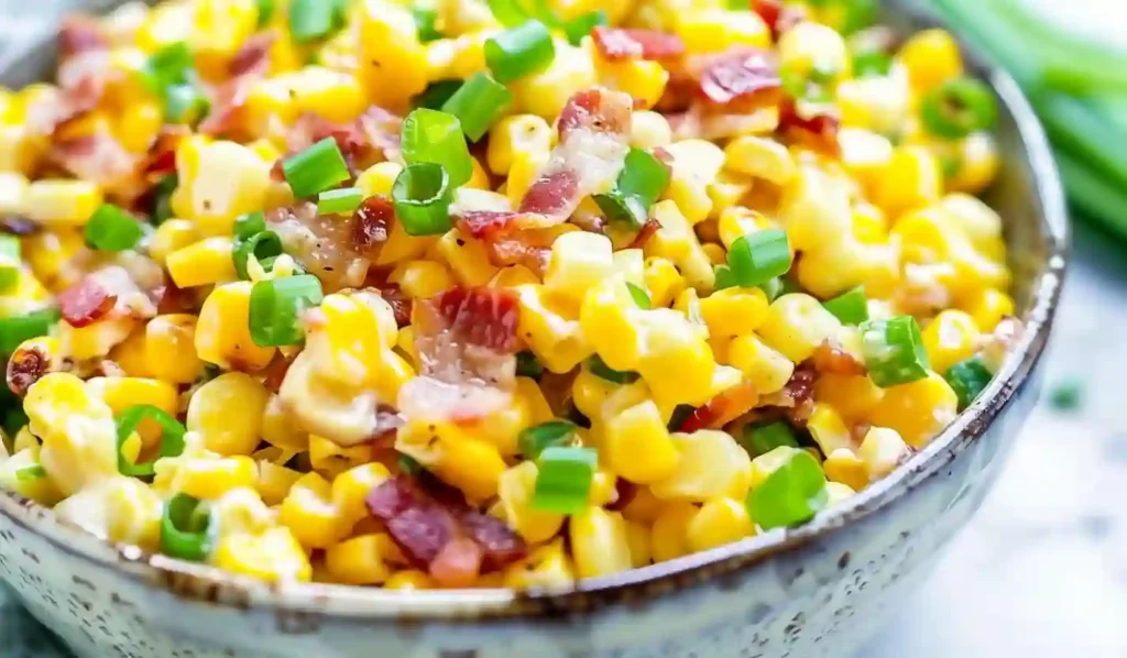 Extra close-up of creamy corn salad with bacon pieces and green onion, in a neutral kitchen background.