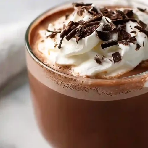 Creamy crockpot hot chocolate topped with whipped cream and chocolate shavings in a glass cup