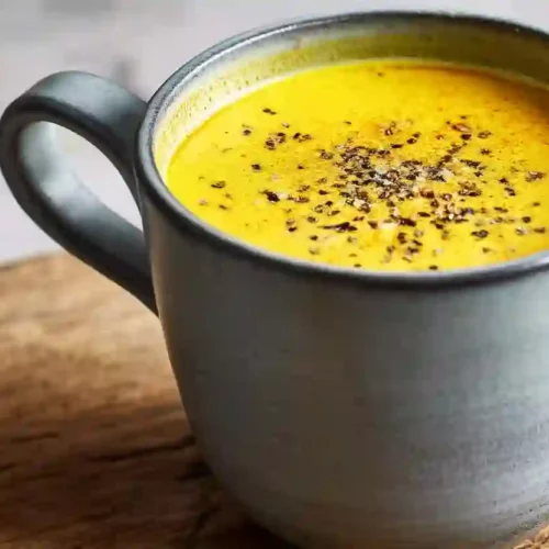 Golden milk in a grey ceramic mug with black pepper on top on a wooden surface