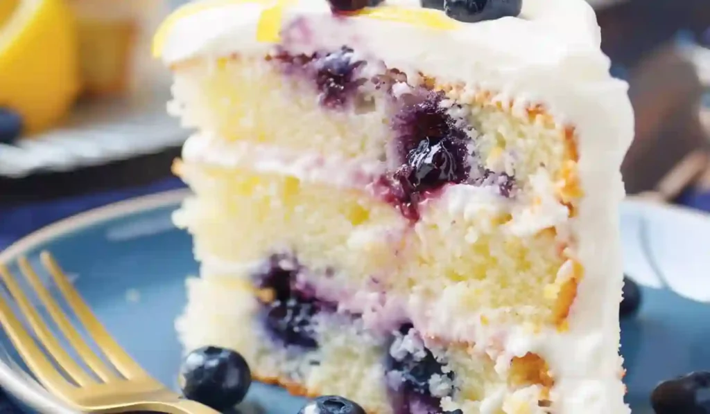 Vertical close-up of a lemon blueberry cake slice with lemon filling and blueberries on a blue plate.