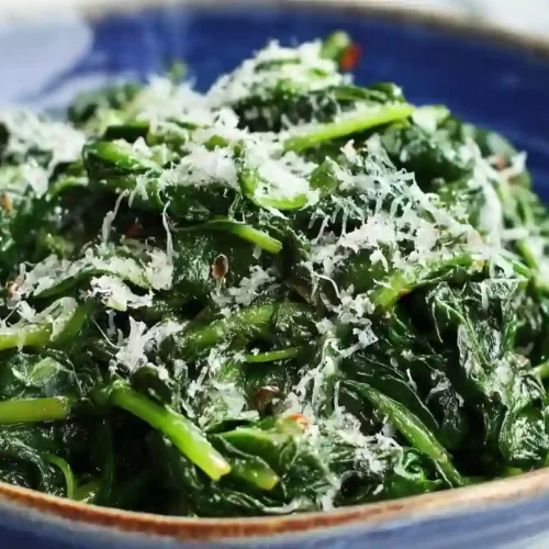Close-up of sautéed spinach in a blue bowl topped with grated cheese
