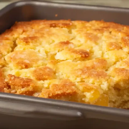Close-up of a golden apricot buckle baked in a square metal pan with a crisp, caramelized surface.