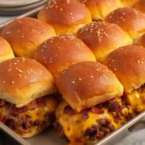 Bacon cheeseburger sliders baked in a pan with melted cheddar cheese and sesame seed buns