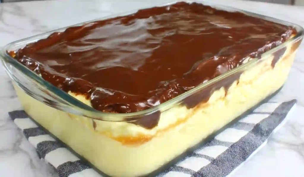 Boston cream pie poke cake in a glass baking dish with vanilla custard layer and glossy chocolate ganache topping