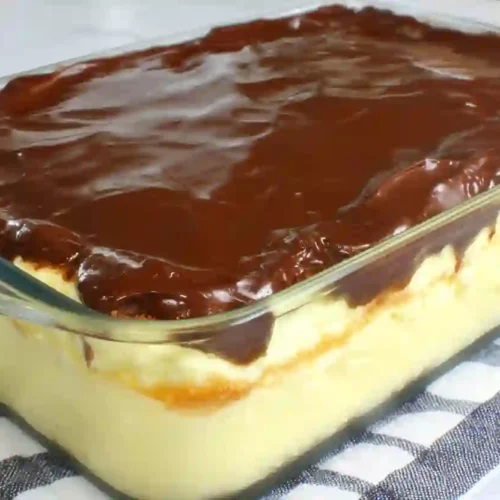 Boston cream pie poke cake in a glass baking dish with vanilla custard layer and glossy chocolate ganache topping