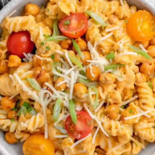 Close-up of buffalo chickpea pasta salad with rotini pasta, roasted chickpeas, cherry tomatoes, green onions, shredded cheese, and creamy buffalo dressing in a gray bowl