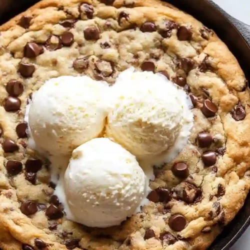 Warm chocolate chip skillet cookie topped with three scoops of vanilla ice cream in a cast iron pan