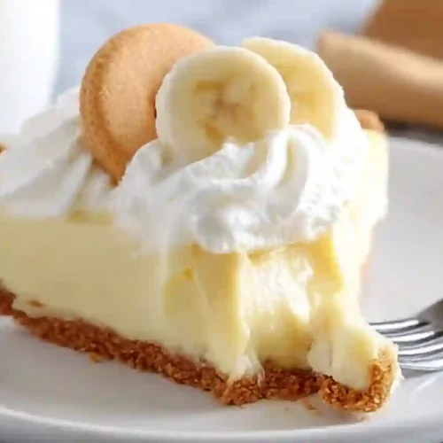 Banana Cream Pie Recipe for Cozy Family Gatherings and Sweet Comfort 3 Slice of banana cream pie topped with whipped cream and banana slice on a white plate
