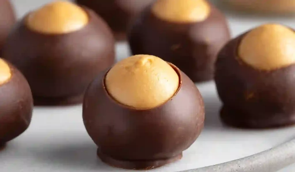Chocolate-dipped peanut butter buckeye candies with exposed peanut butter centers on a clean white surface