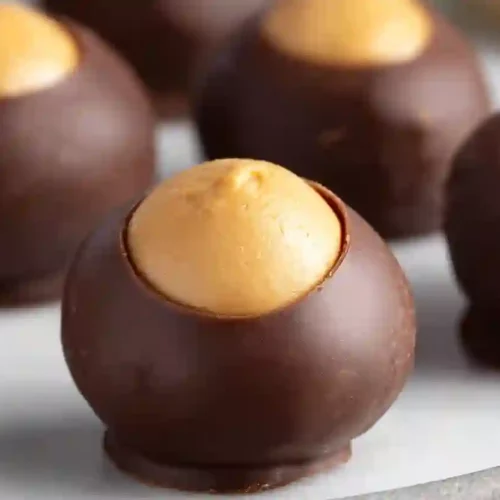 Chocolate-dipped peanut butter buckeye candies with exposed peanut butter centers on a clean white surface