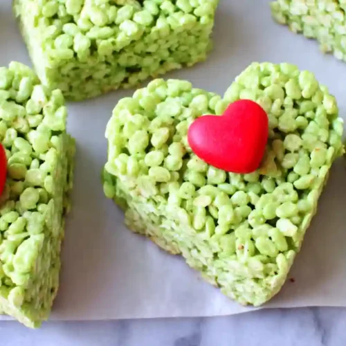 Rice Crispy Treats Recipe – Cozy Holiday Hearts for Sweet Family Moments 3 Green heart-shaped rice krispie treats with small red heart candy on parchment paper