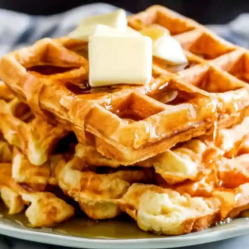 Golden homemade waffles stacked with butter and maple syrup on a plate