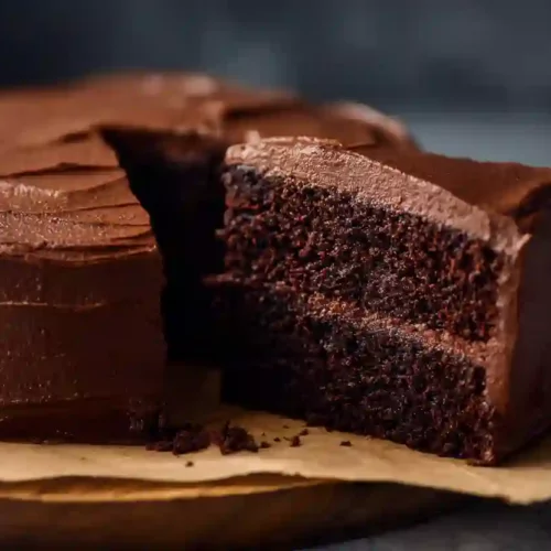 Mini chocolate cake with thick chocolate frosting and one slice cut out, shown in close-up