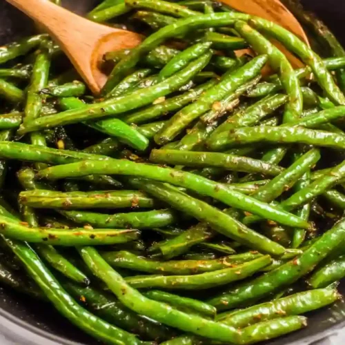 Extra close-up of sautéed green beans cooked until tender and glossy in a dark pan