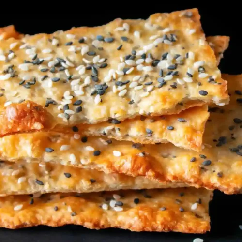 Extra close-up of a golden sourdough discard cracker topped with mixed seeds on a dark background