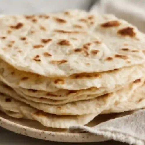 Stack of soft sourdough discard tortillas with light brown spots on a ceramic plate