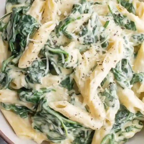Creamy spinach alfredo pasta with penne in a light-colored ceramic bowl, close-up view