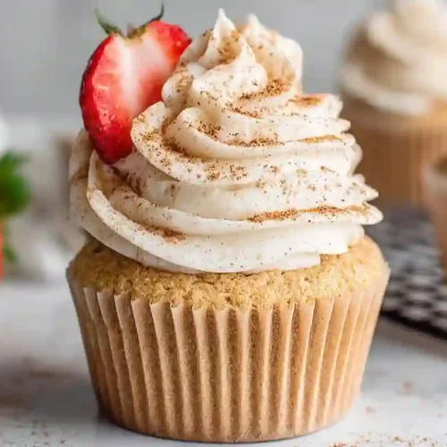 Close-up of a tres leches cupcake topped with whipped cream frosting, cinnamon dusting, and a fresh strawberry slice