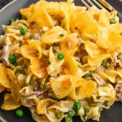 Creamy tuna noodle casserole topped with crushed potato chips and melted cheddar cheese on a dark plate