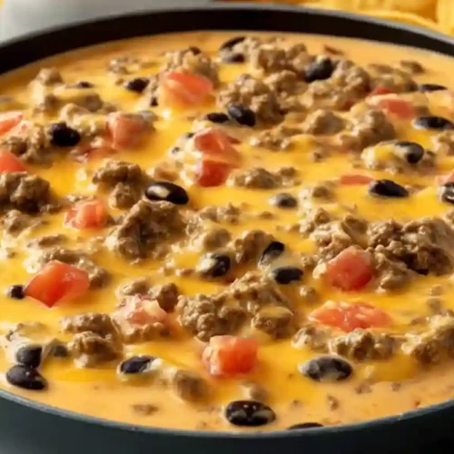 Extra close-up of creamy Velveeta queso dip with ground beef, black beans, and tomatoes in a dark skillet