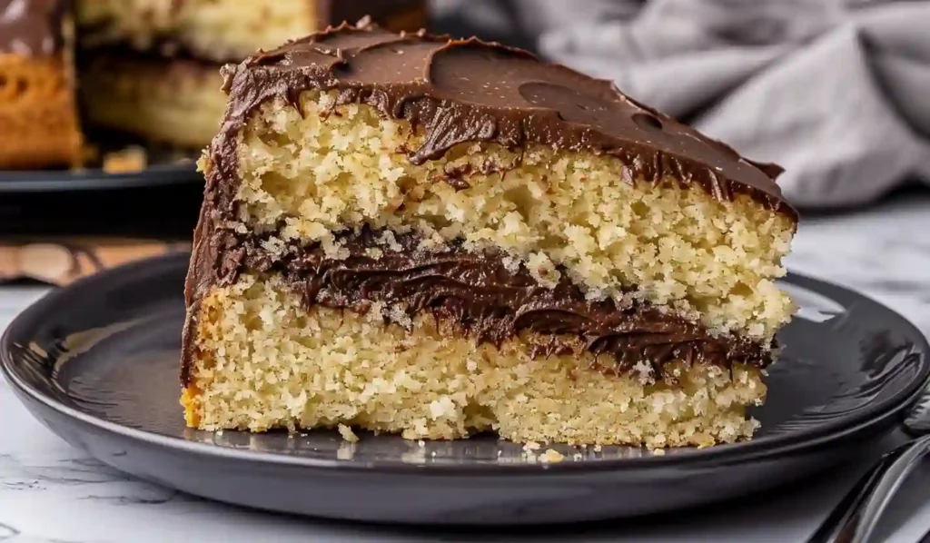 Slice of homemade yellow cake with chocolate frosting on a dark plate