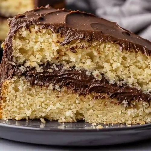 Slice of homemade yellow cake with chocolate frosting on a dark plate