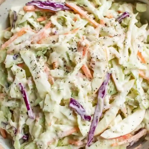 Creamy apple coleslaw with cabbage and carrots served in a rustic ceramic bowl