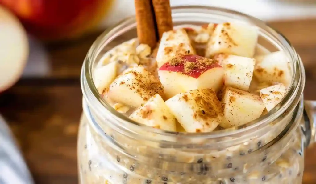 Close-up apple pie overnight oats in a glass jar topped with apple cubes and cinnamon sticks