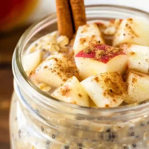 Close-up apple pie overnight oats in a glass jar topped with apple cubes and cinnamon sticks