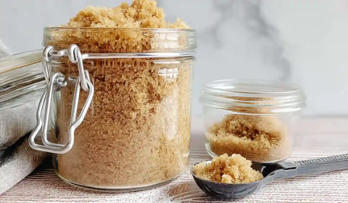 Brown sugar packed in a clear glass jar with a metal clasp on a wooden surface