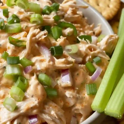 Extra close-up buffalo chicken salad in a light gray bowl with celery sticks and round crackers