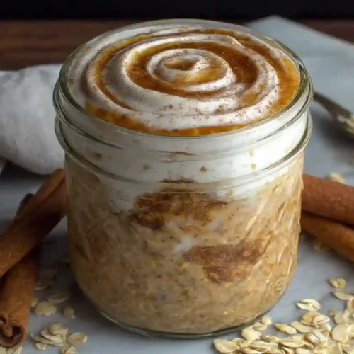 Cinnamon Roll Overnight Oats for Cozy, Protein-Packed Mornings 3 Cinnamon roll overnight oats in a glass jar with creamy cinnamon swirl topping