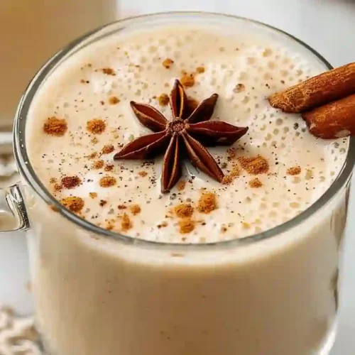 Close-up of creamy homemade eggnog in a clear glass mug topped with cinnamon and star anise