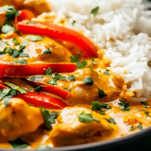 Creamy coconut curry chicken with red peppers served over white rice in a black bowl