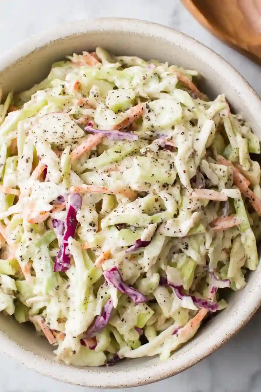 Vertical close-up of creamy apple coleslaw in a rustic ceramic bowl