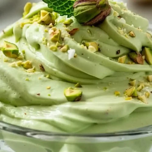Extra close-up of creamy pistachio fluff in a clear glass dessert bowl topped with chopped pistachios and mint