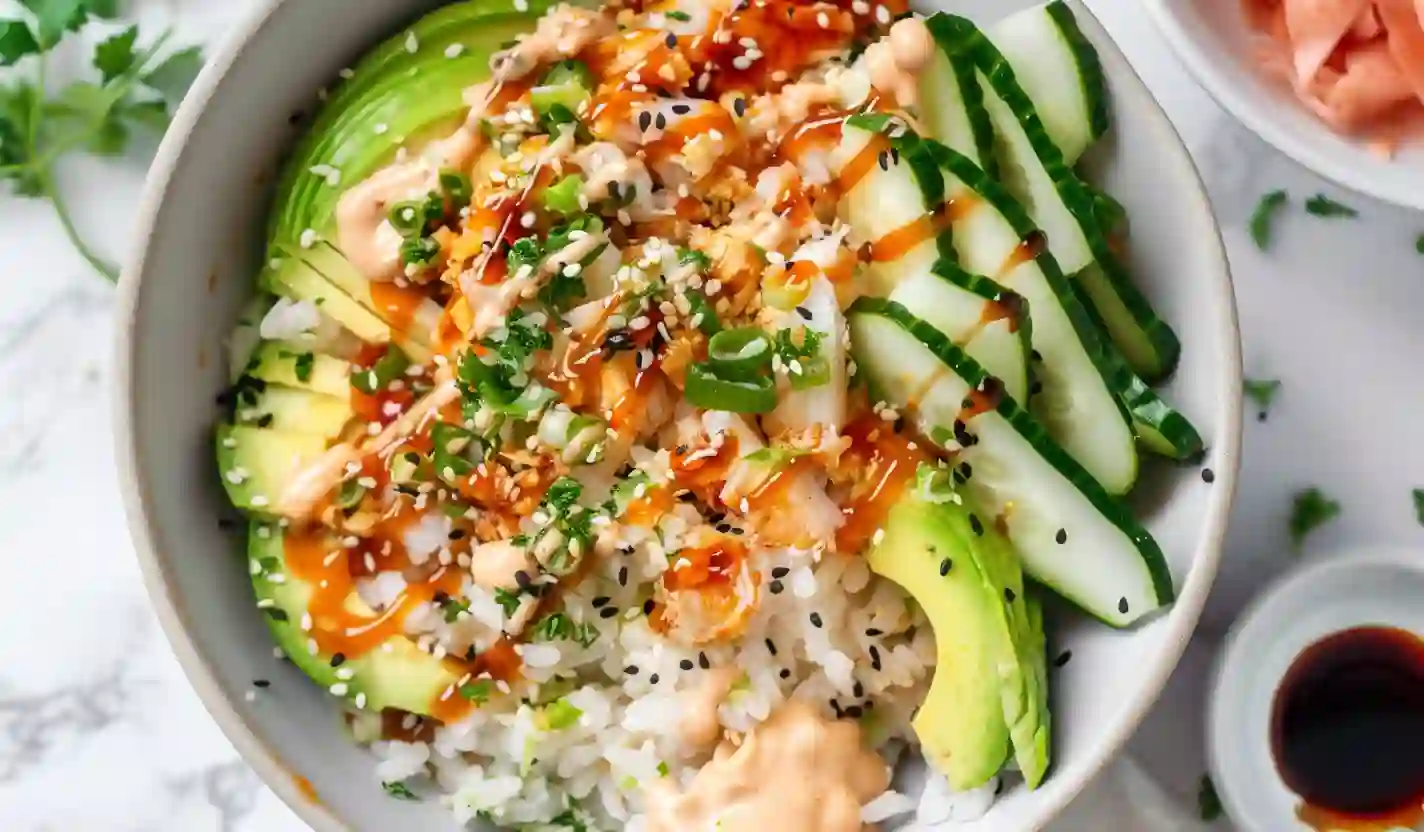 Close-up crunch roll sushi bowl with avocado, cucumber, crab mix, rice, spicy mayo and teriyaki drizzle on marble countertop