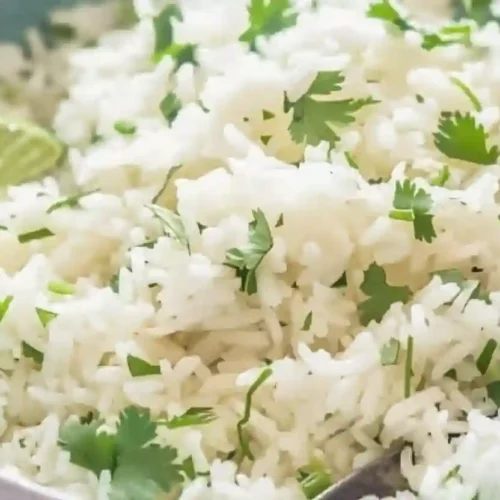 Extra close-up of fluffy lime rice with cilantro in a light blue bowl with a lime slice and spoon
