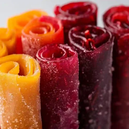 Close-up of colorful homemade fruit leather rolls standing upright in a glass container on a light gray background
